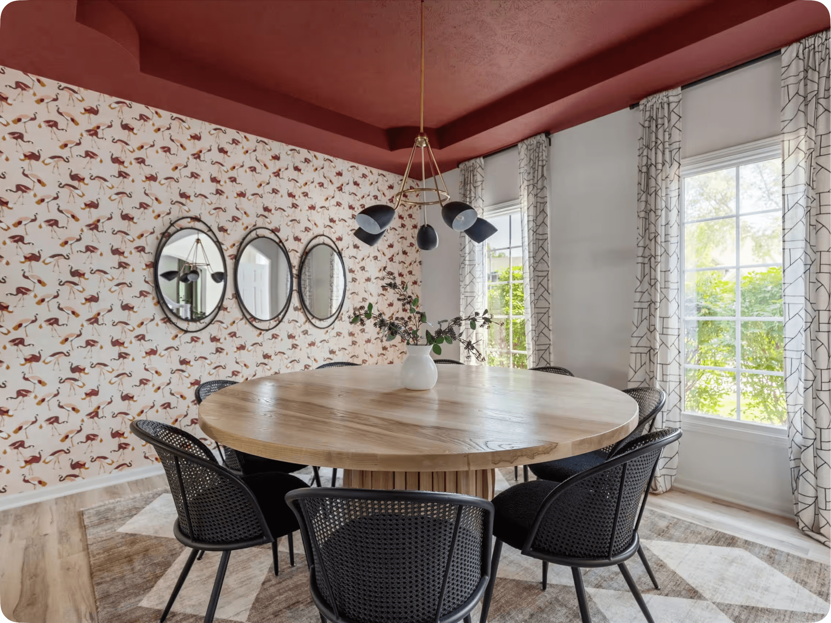 A dining room with flamingo wallpaper, a terracotta ceiling and a round oak table